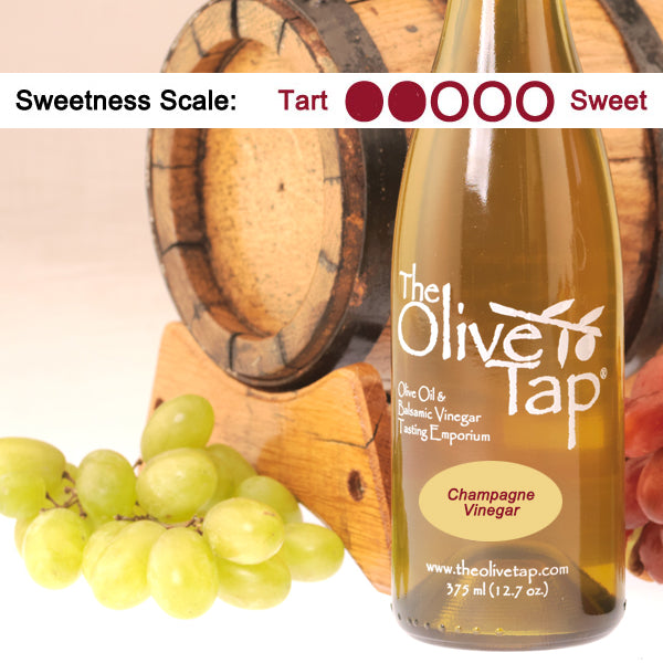 Bottle of The Olive Tap Champagne Vinegar with grapes and a wooden barrel in the background
