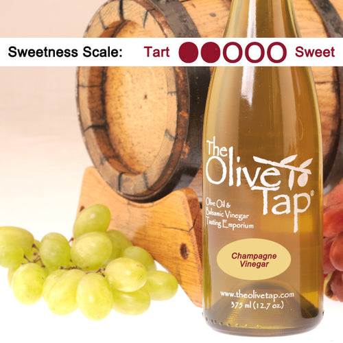 Bottle of The Olive Tap Champagne Vinegar with grapes and a wooden barrel in the background