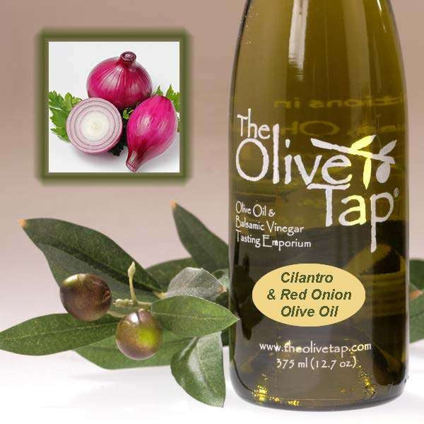 A bottle of Cilantro & Red Onion Olive Oil from The Olive Tap next to olives and leaves with an inset showing red onions and cilantro on a light background.