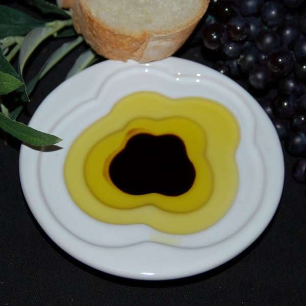 Pinzimonio Olive Oil Dipping Dish - Cloud Design from The Olive Tap with olive oil and vinegar inside and a slice of bread with grapes and olive leaves in the background.