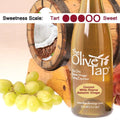 Bottle of Coconut White Riserva Balsamic Vinegar from The Olive Tap with grapes in front of a wooden barrel that has a picture of a coconut inside, indicating a sweetness scale of three.
