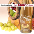 A bottle of Cranberry Pear White Balsamic Vinegar from The Olive Tap surrounded by grapes in front of a wooden barrel with pears and cranberries inside, and a sweetness scale indicating a three on a light background.