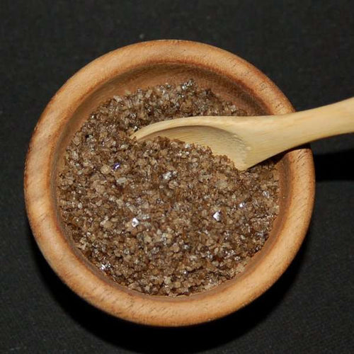 Durango Hickory Smoked Sea Salt from The Olive Tap: Brown grains of sea salt in a wooden bowl and a wooden spoon against a black background.