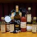 Garlic Lovers Gift Box from The Olive Tap:  a collection of various garlic products including oils, vinegar, condiments, salts, and more on a wooden surface with grapes in the background.
