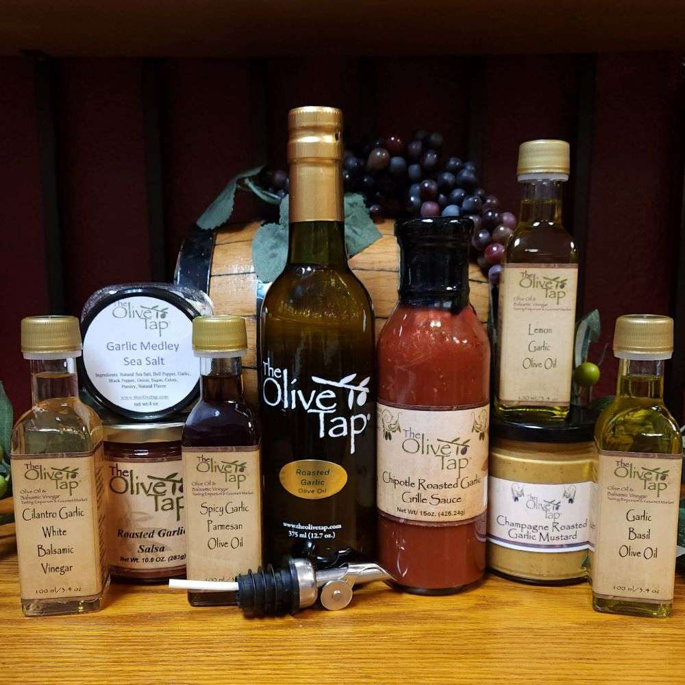 Garlic Lovers Gift Box from The Olive Tap:  a collection of various garlic products including oils, vinegar, condiments, salts, and more on a wooden surface with grapes in the background.