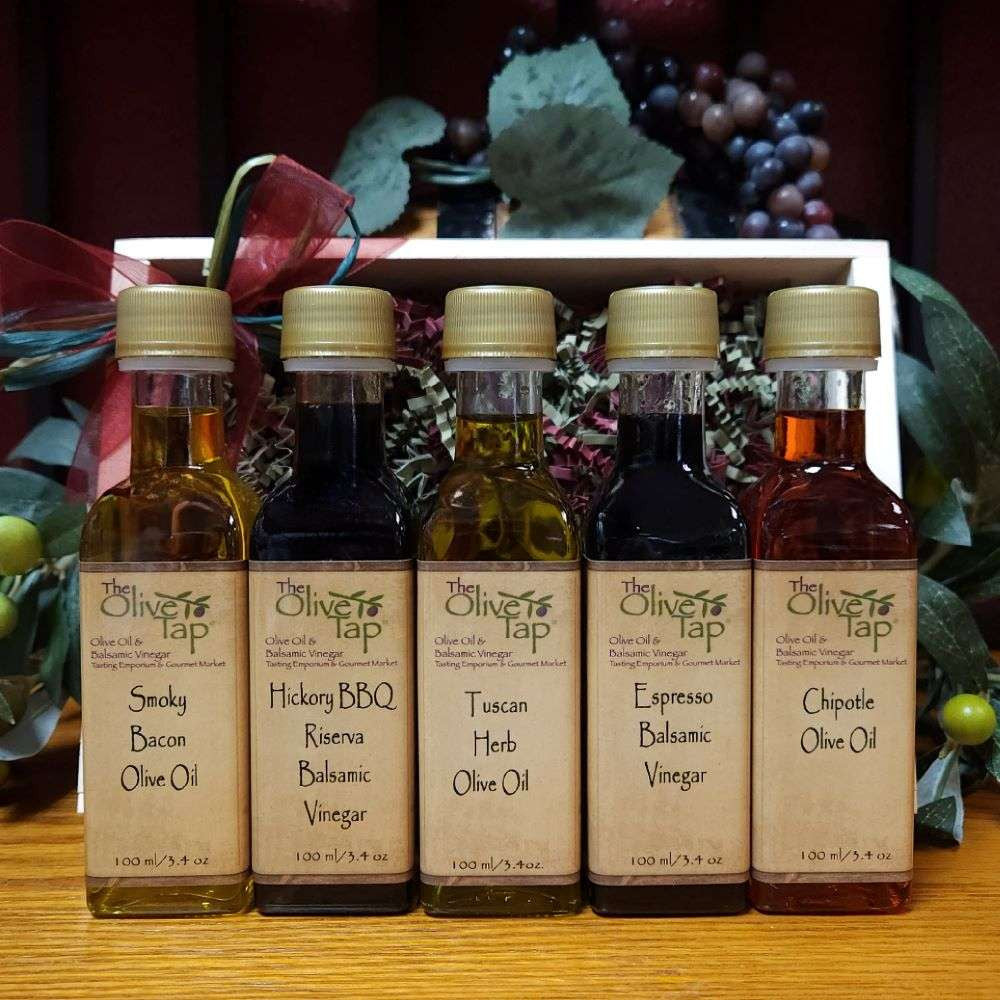 Great for Grilling Sampler Set from The Olive Tap:  Five bottles of olive oils and vinegars in front of a wooden crate with a bow with grapes in the background on a wooden surface.