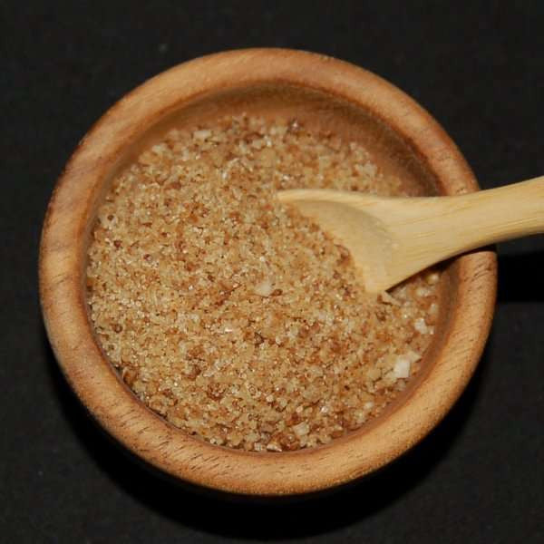 Habanero Pepper Sea Salt from The Olive Tap: A wooden bowl of brown grains of sea salt with a wooden spoon against a black background.