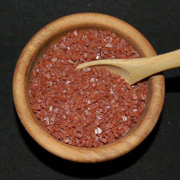 Hawaiian Red Sea Salt from The Olive Tap: Pebble-sized red pieces of sea salt  in a wooden bowl with a wooden spoon against a black background.