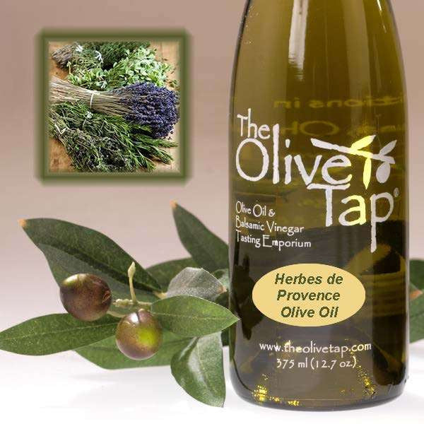 A bottle of Herbes de Provence Olive Oil from The Olive Tap next to olives and leaves with an inset showing fresh herbs.