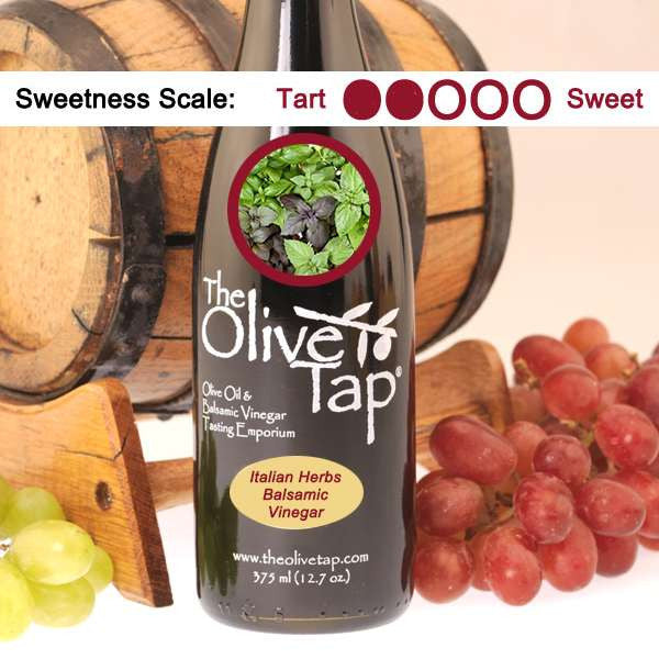 A bottle of Italian Herbs Balsamic Vinegar from The Olive Tap with a picture of fresh basil, surrounded by grapes in front of a wooden barrel, and a sweetness scale indicating a two on a light background.