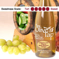 A bottle of Jalapeno Lime Riserva White Balsamic Vinegar surrounded by grapes in front of a wooden barrel with limes and jalapenos inside, and a sweetness scale indicating a five on a light background.