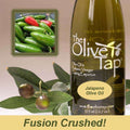 A bottle of The Olive Tap Jalapeno Olive Oil next to olives and leaves with inset of fresh jalapenos and the words "fusion crushed!" at the bottom of the picture.