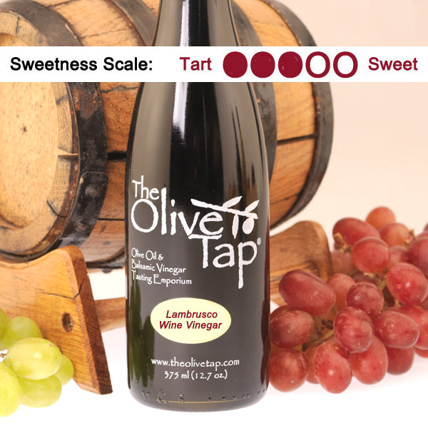 Bottle of The Olive Tap Lambrusco Wine Vinegar with grapes and barrels in the background