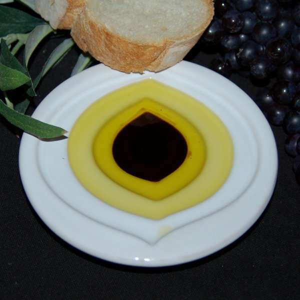 Pinzimonio Olive Oil Dipping Dish - Leaf Design from The Olive Tap with olive oil and vinegar inside and a slice of bread with grapes and olive leaves in the background.