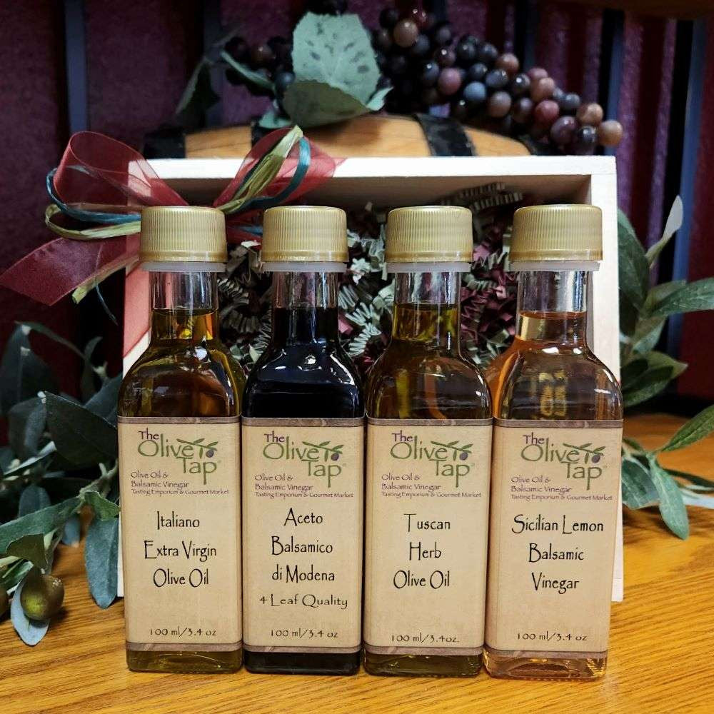 Olive Tap Little Italy sampler: Two olive oil and two vinegar bottles in front of a wooden crate with a bow and purple grapes in the background.