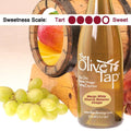 A bottle of Mango White Riserva Balsamic Vinegar from The Olive Tap surrounded by grapes in front of a wooden barrel with a picture of a mango inside, and a sweetness scale indicating a four on a light background.