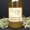 A bottle of Margarita Key Lime Grilling Sauce from The Olive Tap with green crinkle paper against a black background.