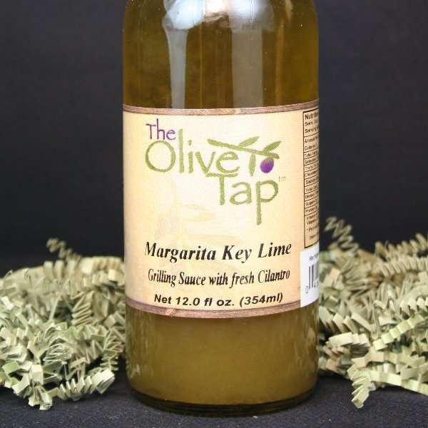 A bottle of Margarita Key Lime Grilling Sauce from The Olive Tap with green crinkle paper against a black background.