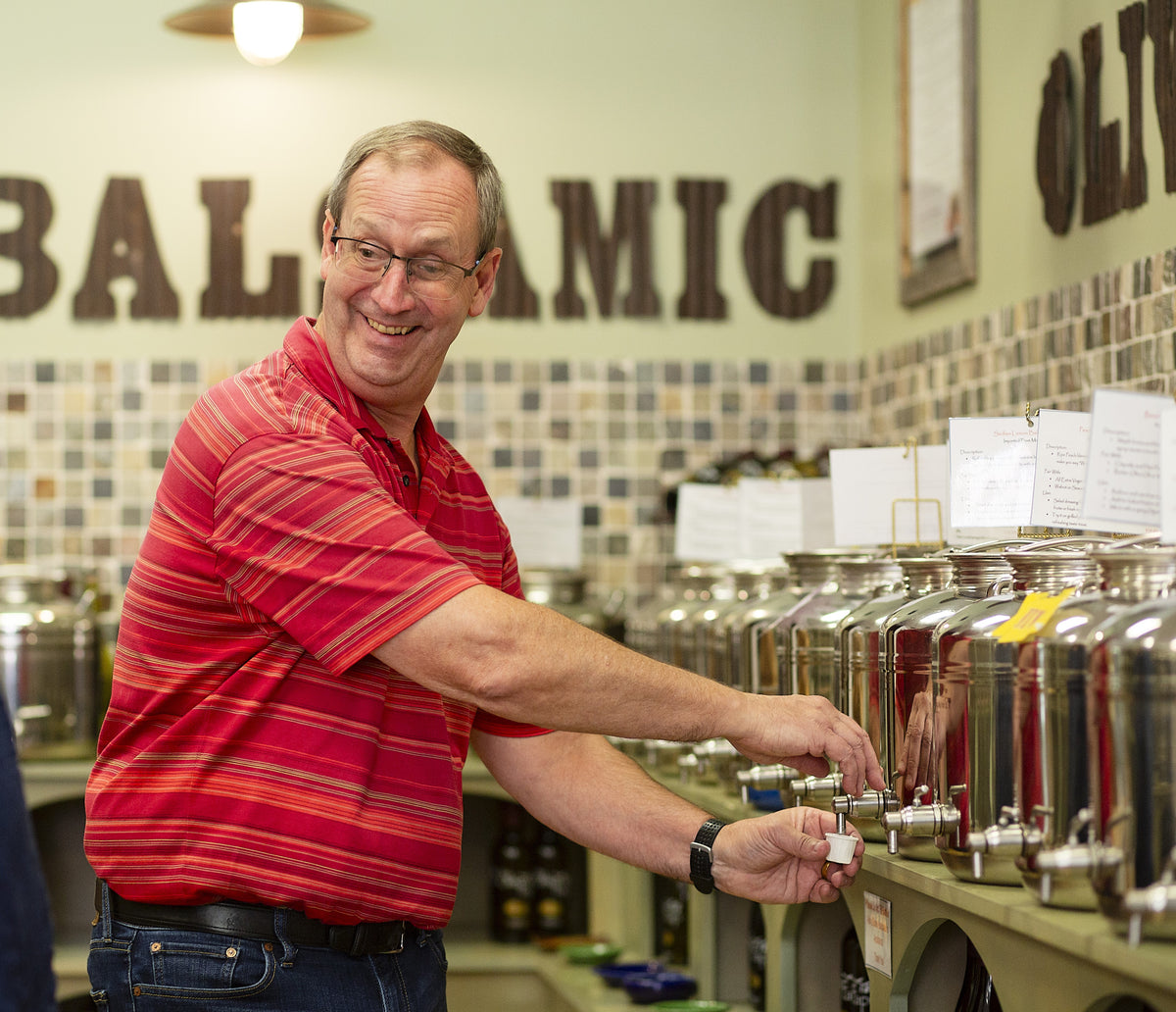 Mike, the owner of The Olive Tap, dispensing olive oil in a small cup with silver tanks