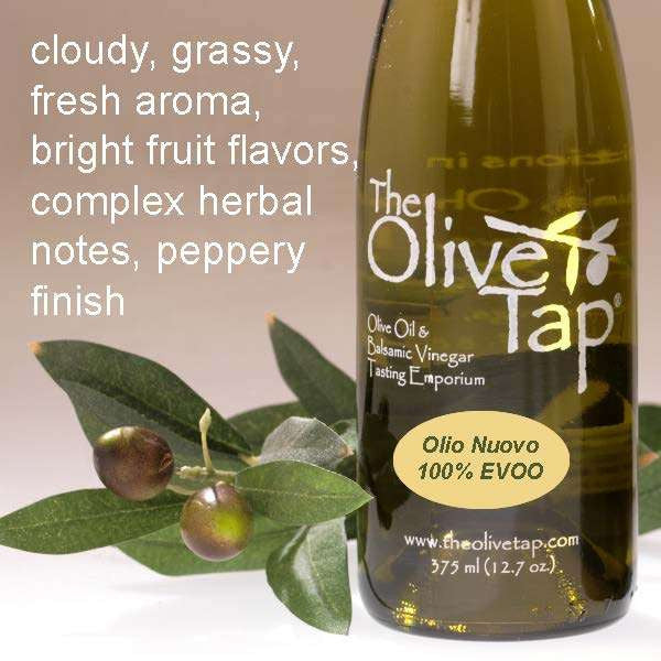 A bottle of Olio Nuovo 100% Extra Virgin Olive Oil from The Olive Tap with olives and leaves including text describing the olive oil flavor profile on a light background.