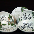 A set of Olive Oil Dipping Bowls from The Olive Tap decorated with writing and olive leaves and branches, displayed on a black background.