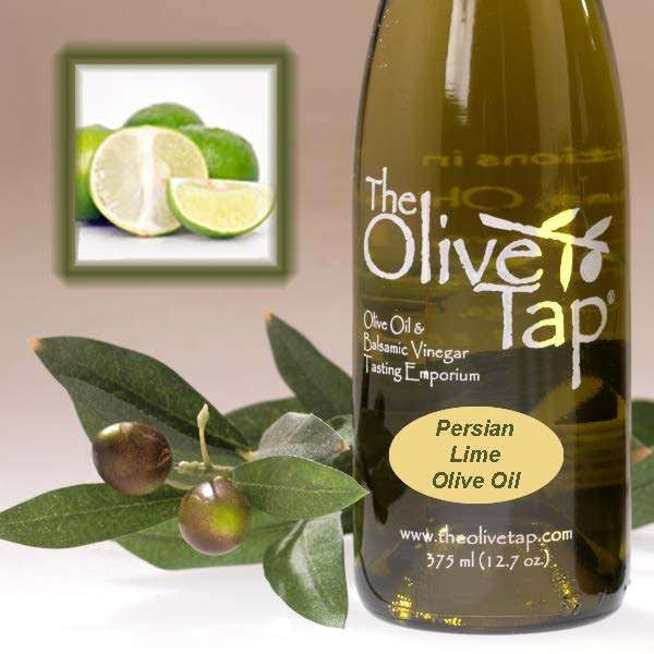 A bottle of Persian Lime Olive Oil from The Olive Tap next to olives and leaves with an inset showing fresh limes.