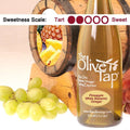 A bottle of Pineapple White Balsamic Vinegar from The Olive Tap with grapes in front of a wooden barrel with a picture of pineapple and a sweetness scale indicating a two.