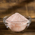 Pink Himalayan Salt from The Olive Tap in a clear glass bowl on a wooden surface.