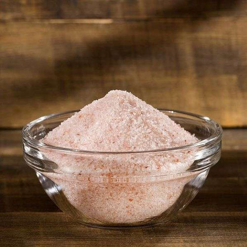 Pink Himalayan Salt from The Olive Tap in a clear glass bowl on a wooden surface.