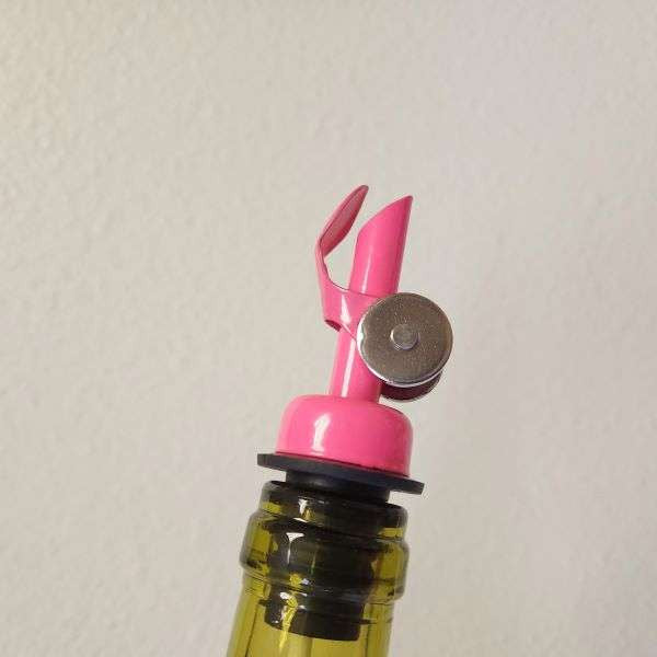 Limited Edition Pink Pour Spout from The Olive Tap inside the opening of a glass bottle in front of a white background.