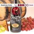 A bottle of Pomegranate Balsamic Vinegar from The Olive Tap with a picture of sliced pomegranate, surrounded by grapes in front of a wooden barrel, and a sweetness scale indicating a three.