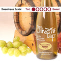 A bottle of Premium White Balsamic Vinegar from The Olive Tap with grapes in front of a wooden barrel and a sweetness scale indicating a one.