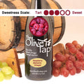 A bottle of Raspberry Balsamic Vinegar from The Olive Tap surrounded by grapes in front of a wooden barrel, and a sweetness scale indicating a three.