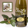 A bottle of Roasted Garlic Olive Oil from The Olive Tap next to olives and leaves with an inset showing bulbs of fresh garlic.