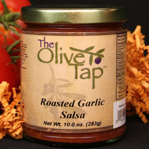 A jar of Roasted Garlic Salsa from The Olive Tap surrounded by tomatoes and orange crinkle paper against a black background.