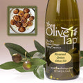 A bottle of Roasted Onion Olive Oil from The Olive Tap next to olives and leaves with an inset showing roasted onions on a light background.
