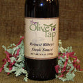 Robust Ribeye Steak Sauce from The Olive Tap on a brown backdrop surrounded by red and green decorative crinkle paper.
