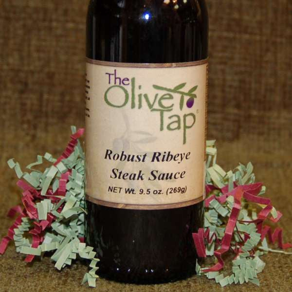 Robust Ribeye Steak Sauce from The Olive Tap on a brown backdrop surrounded by red and green decorative crinkle paper.