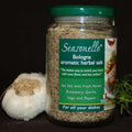 Jar of Seasonello® Herbal Sea Salt, a staff favorite from The Olive Tap, next to fresh rosemary and a bulb of garlic on a black background.