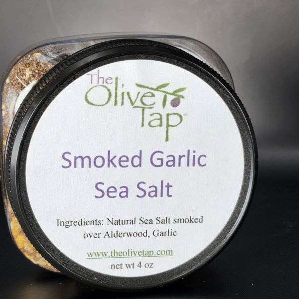 Smoked Garlic Sea Salt in a jar from The Olive Tap with a white label that includes The Olive Tap logo, product name, and ingredients list, with the jar in front of a gray background.