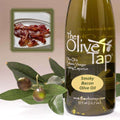 A bottle of Smoky Bacon Olive Oil from The Olive Tap next to olives and leaves with an inset showing bacon on a light background.
