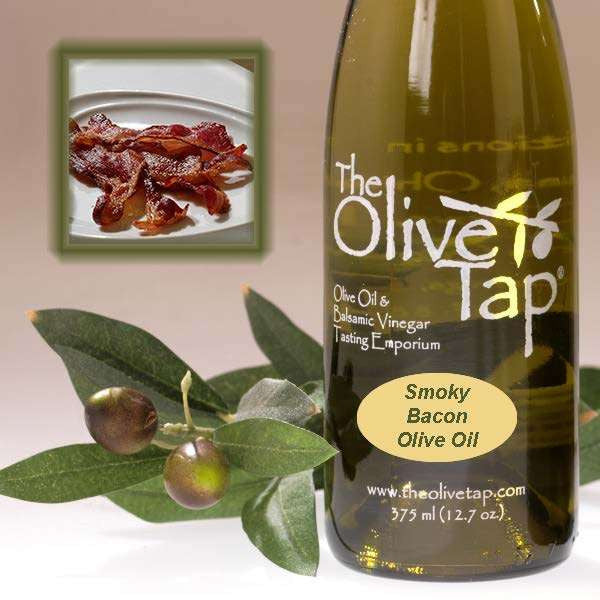 A bottle of Smoky Bacon Olive Oil from The Olive Tap next to olives and leaves with an inset showing bacon on a light background.
