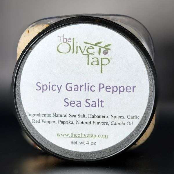 Spicy Garlic Pepper Sea Salt jar from The Olive Tap with a white label that includes The Olive Tap logo with an olive branch, product name, and ingredients list with the jar in front of a gray background.