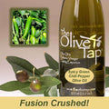 A bottle of Spicy Green Chili Pepper Olive Oil from The Olive Tap next to olives and leaves with an inset showing green chilis on a light background with the words "fusion crushed!" at the bottom.