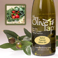 A bottle of Spicy Tuscan Olive Oil from The Olive Tap next to olives and leaves with an inset showing spicy peppers and fresh herbs on a light background.