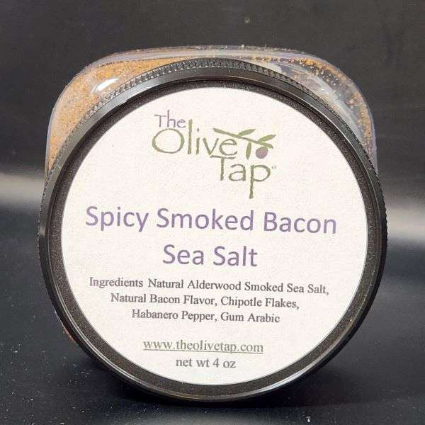 Spicy Smoked Bacon Sea Salt in jar from The Olive Tap with a white label that includes The Olive Tap logo with an olive branch, product name, and ingredients list, with the jar in front of a gray background.