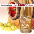 Strawberry White Balsamic Vinegar from The Olive Tap surrounded by grapes in front of a wooden barrel with strawberries inside, and a sweetness scale indicating a three on a light background.