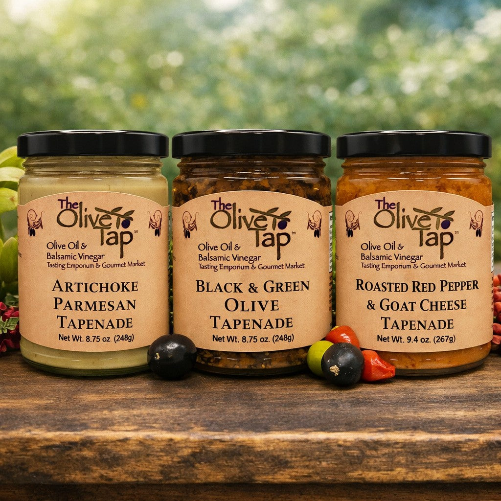 Three jars of Olive Tap tapenades on a wooden surface with a blurred green background and fresh olives in front of the jars.