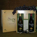Taste of Italy Gift Box from The Olive Tap: one bottle of olive oil and one bottle of balsamic vinegar in a decorative Olive Tap box with purple grapes on top of it, divided by a piece of cardboard with a description of each product, and two metal pour spouts crossed in front of the box.