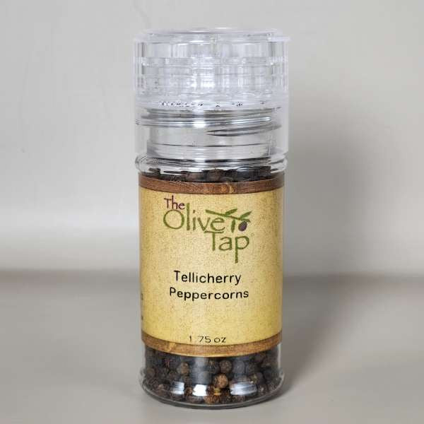 Container of Tellicherry Peppercorns by The Olive Tap in a jar with a grinder lid with The Olive Tap logo and olive branch on a neutral background.